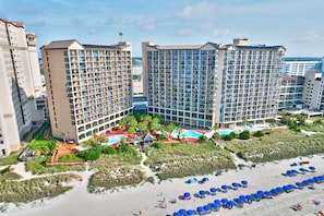 Ein Hotel mit mehreren Hochhäusern, einem Strandbereich mit Sonnenschirmen und einem Pool.