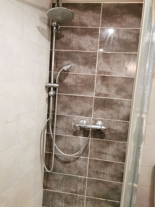 A shower with a handheld showerhead and a wall-mounted faucet.