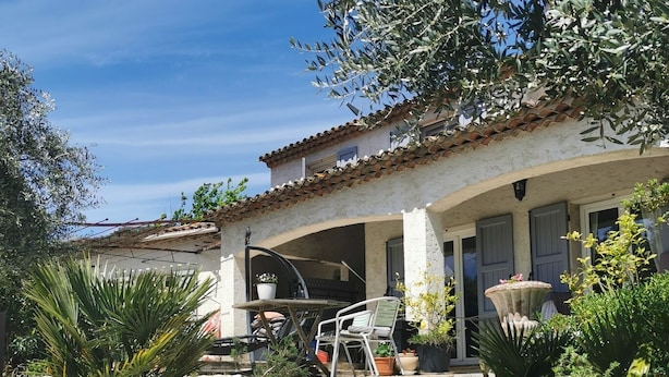 Una scala in pietra conduce a una zona esterna coperta con tavolo e sedie da patio, immersa nel verde e affiancata da un edificio con tetto in tegole.