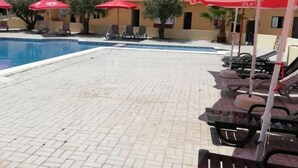 A swimming pool with lounge chairs and red umbrellas.