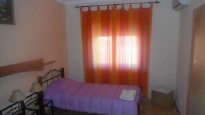 A bedroom with a bed, a nightstand, a lamp, and a window with orange curtains.