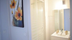 Un baño con lavamanos blanco, espejo y ducha con persianas horizontales.