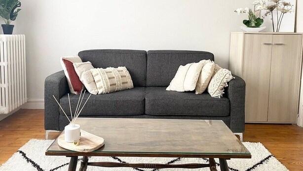 Una sala de estar con un sofá gris, una mesa de centro de vidrio y decoración en la pared.