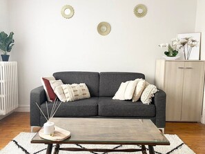 Een woonkamer met een grijze bank, een glazen salontafel en decoratieve wandkunst.