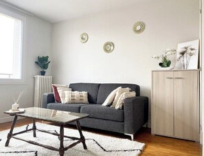 Een woonkamer met een grijze bank, een glazen salontafel, een wit tapijt en een houten kast.