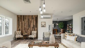 A spacious living room with a wooden accent wall, a large window, and a cozy seating area with a sofa and chairs. - Nature Lodge - Dreamer - with Hiwassee River Access (Calhoun)