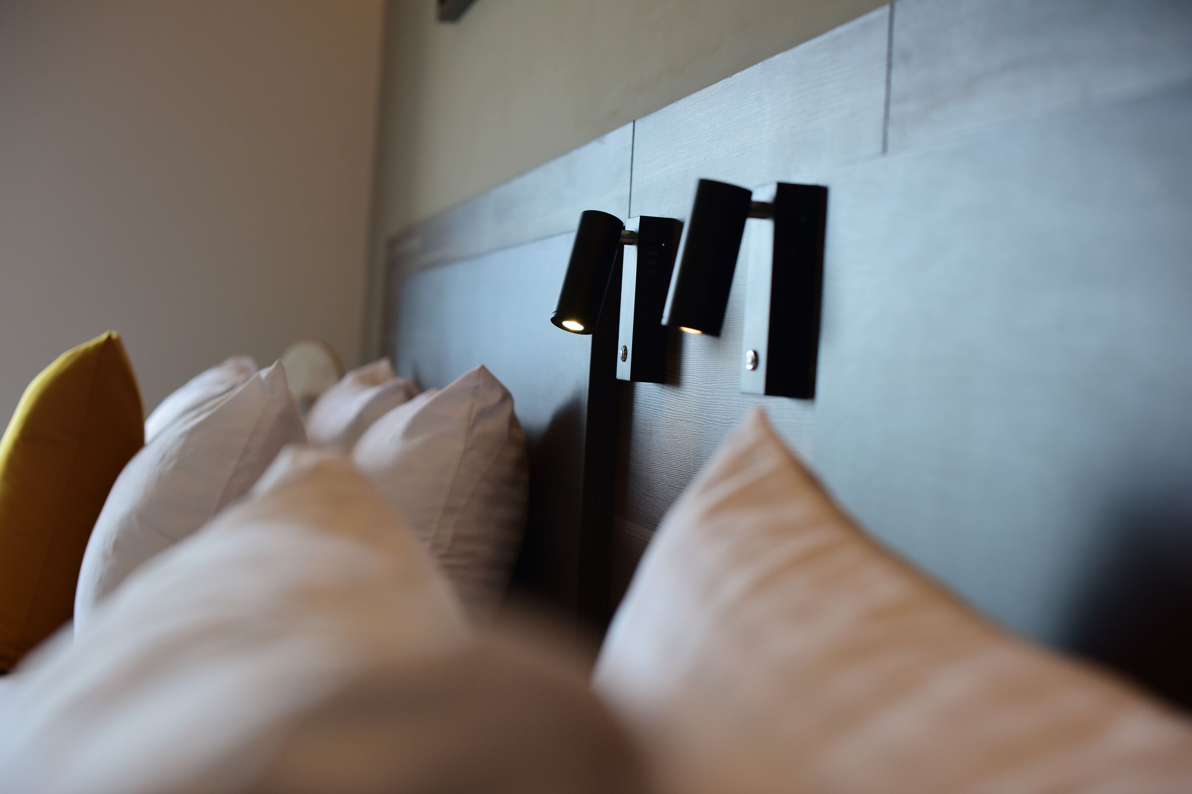 Una cama con almohadas blancas y un cabecero con una lámpara moderna.