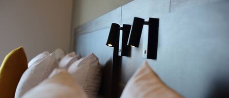 Una cama con almohadas blancas y un cabecero con una lámpara moderna.