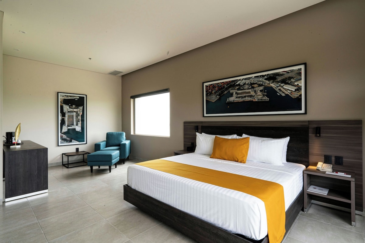 Een hotelkamer met een groot bed, een bureau, een stoel, een raam en kunstwerken aan de muren.