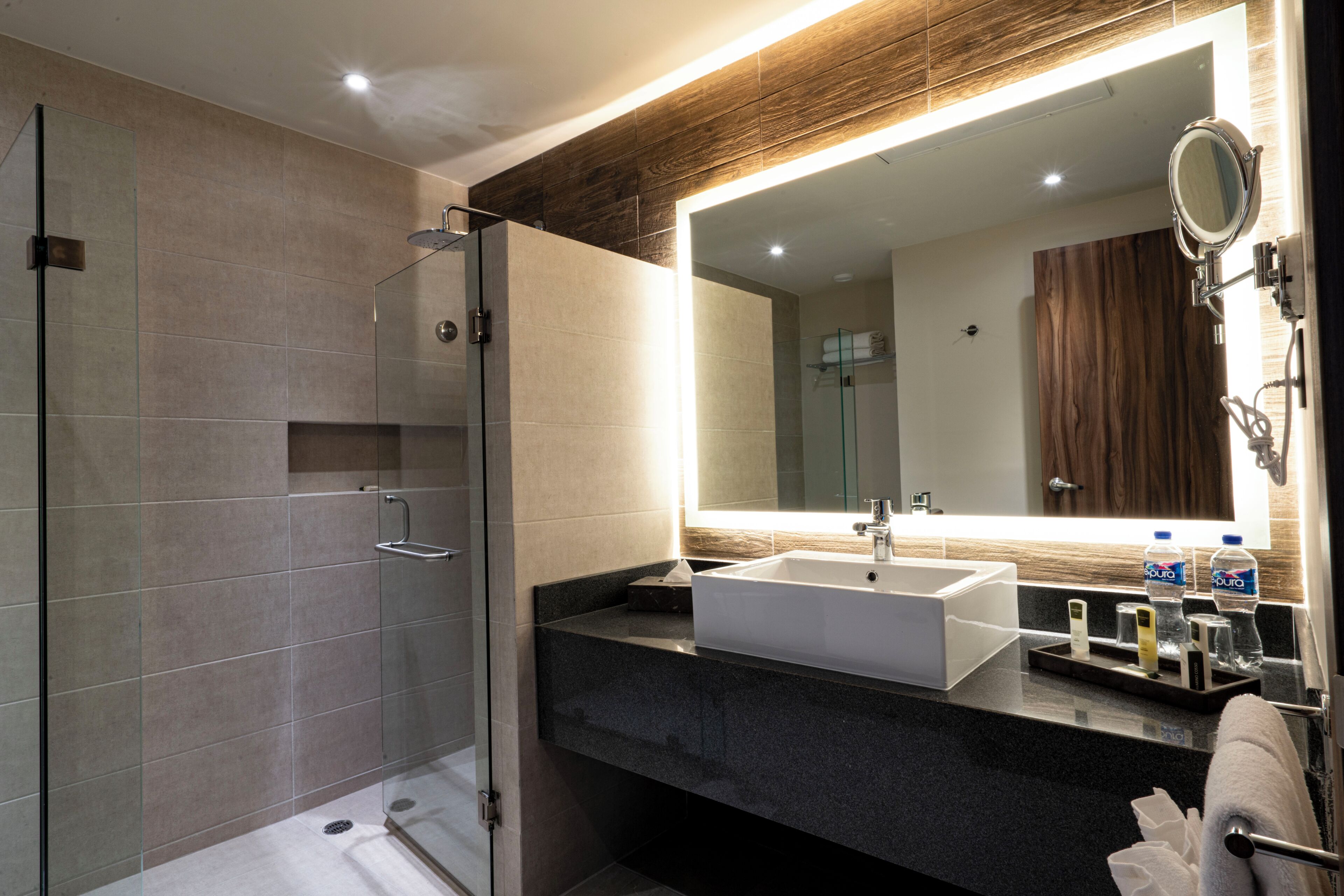 Un baño moderno con cabina de ducha de vidrio, un espejo grande, un lavabo blanco y una encimera oscura.