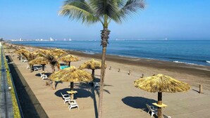 A beach with palm trees, thatched umbrellas, and white lounge chairs. - Delta Hotels by Marriott Riviera Veracruz (Alvarado)