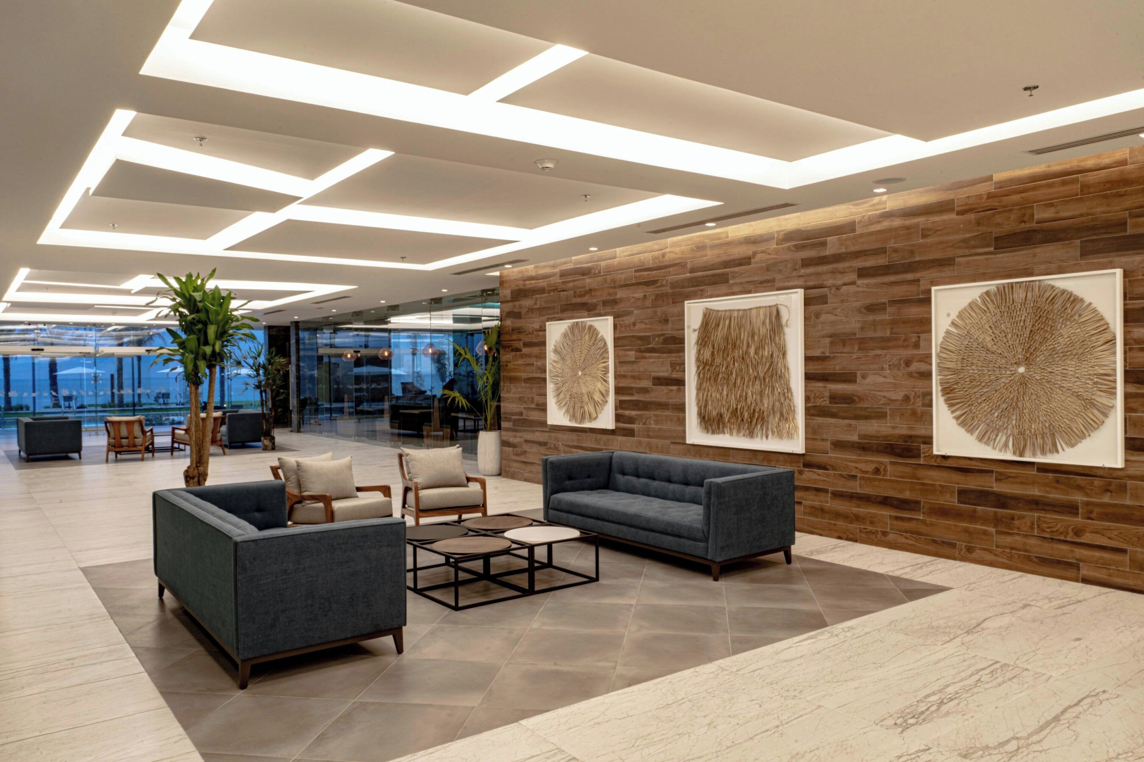 A modern lobby with a wooden wall, two sofas, a coffee table, and a potted plant.