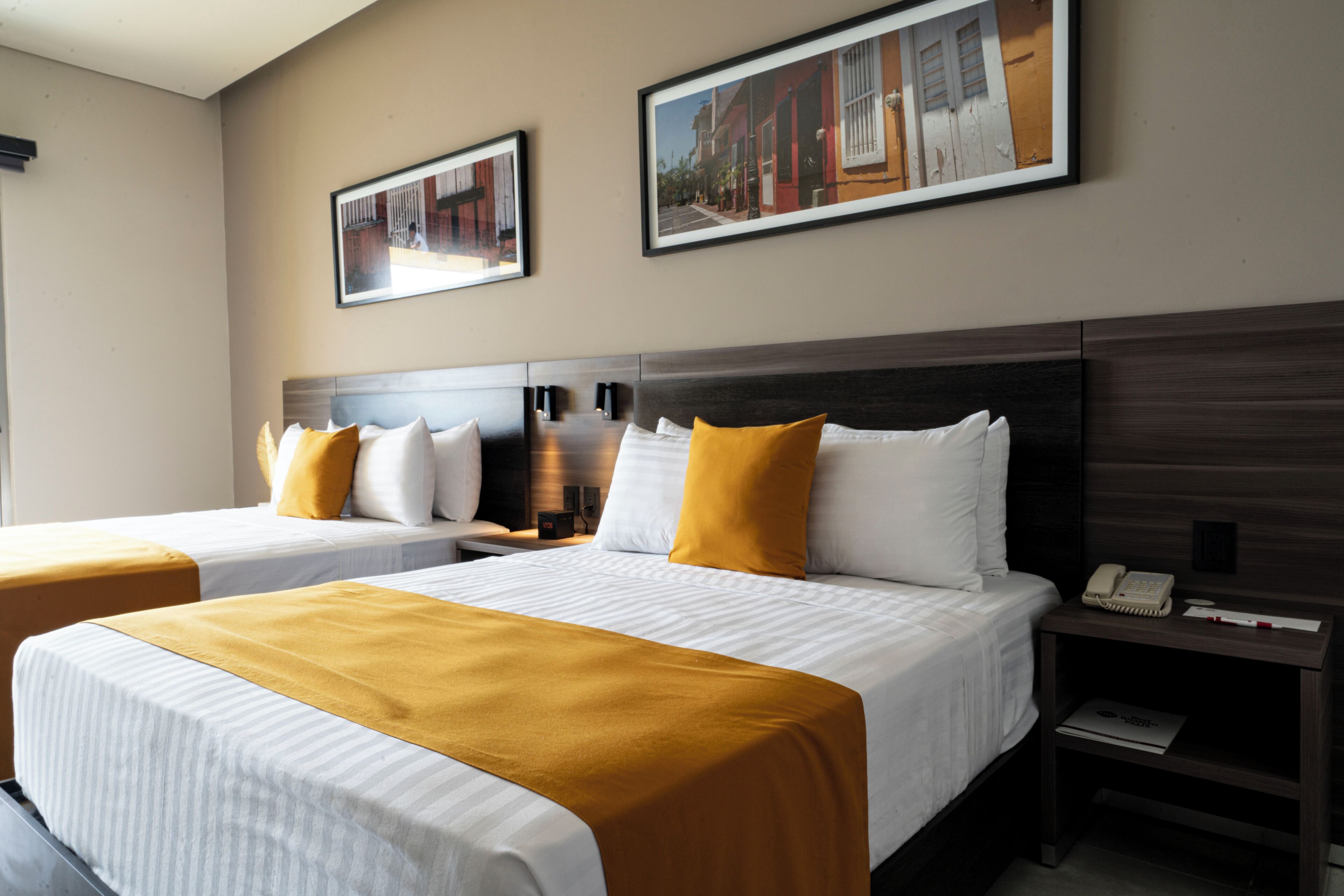 Ein Hotelzimmer mit zwei Betten, einem Nachttisch mit Telefon und gerahmten Bildern an der Wand.