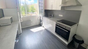 A modern kitchen with white cabinets, a built-in oven, and a window with a view of the outside. - Grand T2 Lumineux Pied du Métro et Centre de Lyon (Villeurbanne)