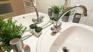 A bathroom with a large white sink, two faucets, and a towel rack. There are small potted plants on the counter. - Grand T2 Lumineux Pied du Métro et Centre de Lyon (Villeurbanne)