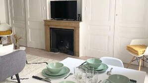 En matplats med ett vitt bord dukat för fyra personer, gröna tallrikar och bestick. En tv är monterad ovanför en öppen spis.