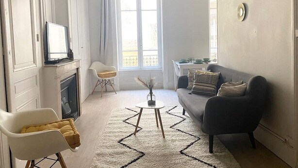 Ett vardagsrum med en soffa, ett soffbord och en tv. Det finns en öppen spis, ett fönster och en dörr.
