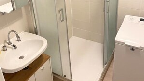 Ett badrum med en dusch som är avskärmad med glasväggar, ett handfat med spegel och en liten vit apparat, troligen en värmare eller torktumlare.