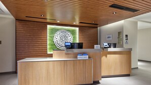 Ein Hotel-Empfangsbereich mit einem hölzernen Empfangstresen, einer digitalen Check-in-Kiosk und einer Wand mit einem kreisförmigen Muster.