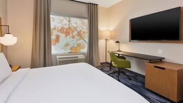 A hotel room with a large bed, a desk with a chair, a flat-screen TV, and a window with curtains.