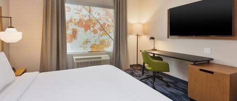 A hotel room with a large bed, a desk with a chair, a flat-screen TV, and a window with curtains.