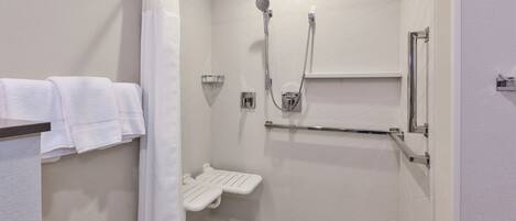 Un área de ducha moderna con un cabezal de ducha manual, una cabina de ducha con puerta de cristal y un perchero blanco.