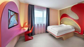 A modern hotel room with a bed, a desk, and a TV screen displaying a welcome message.