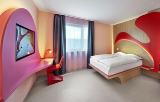 A modern hotel room with a bed, a desk, and a TV screen displaying a welcome message.