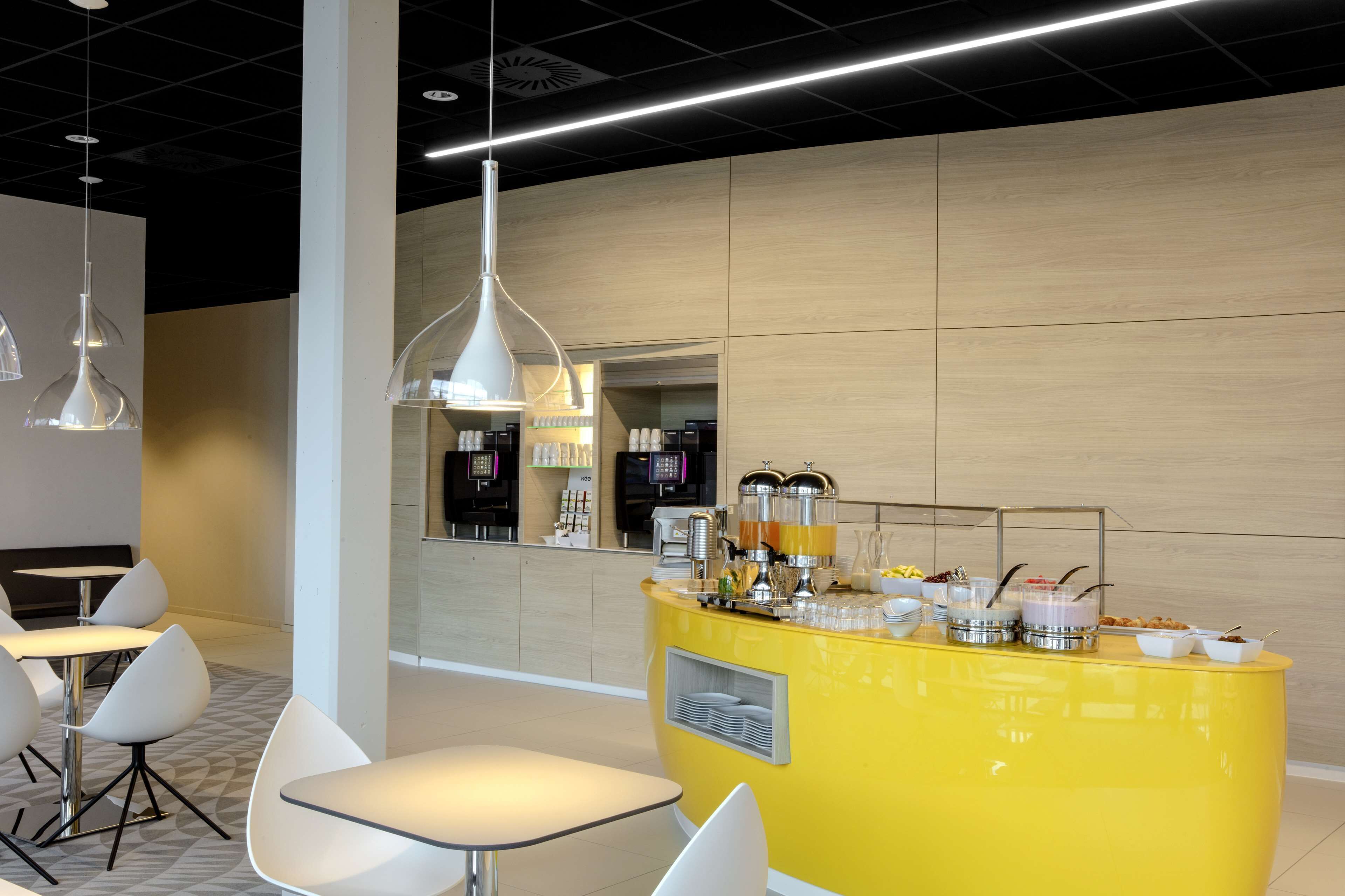 Un café moderno con mostrador amarillo, sillas blancas y lámparas colgantes.
