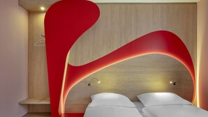 A modern bedroom with a wooden headboard, a red accent wall, and two beds. - Prize by Radisson, Munich Airport (Hallbergmoos)