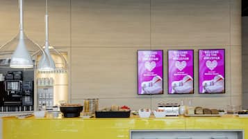 A reception area with a yellow counter, coffee machines, and a wall-mounted TV displaying a welcome message.