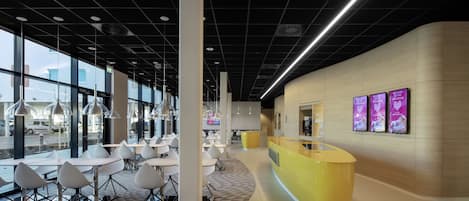 Un interior moderno con mostrador de recepción, zona de estar y grandes ventanales que ofrecen vistas al exterior.