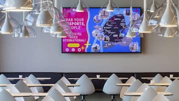 Un moderno vestíbulo de hotel con una gran pantalla digital que muestra un mapa, diversas zonas de estar con sillas originales e iluminación colgante.