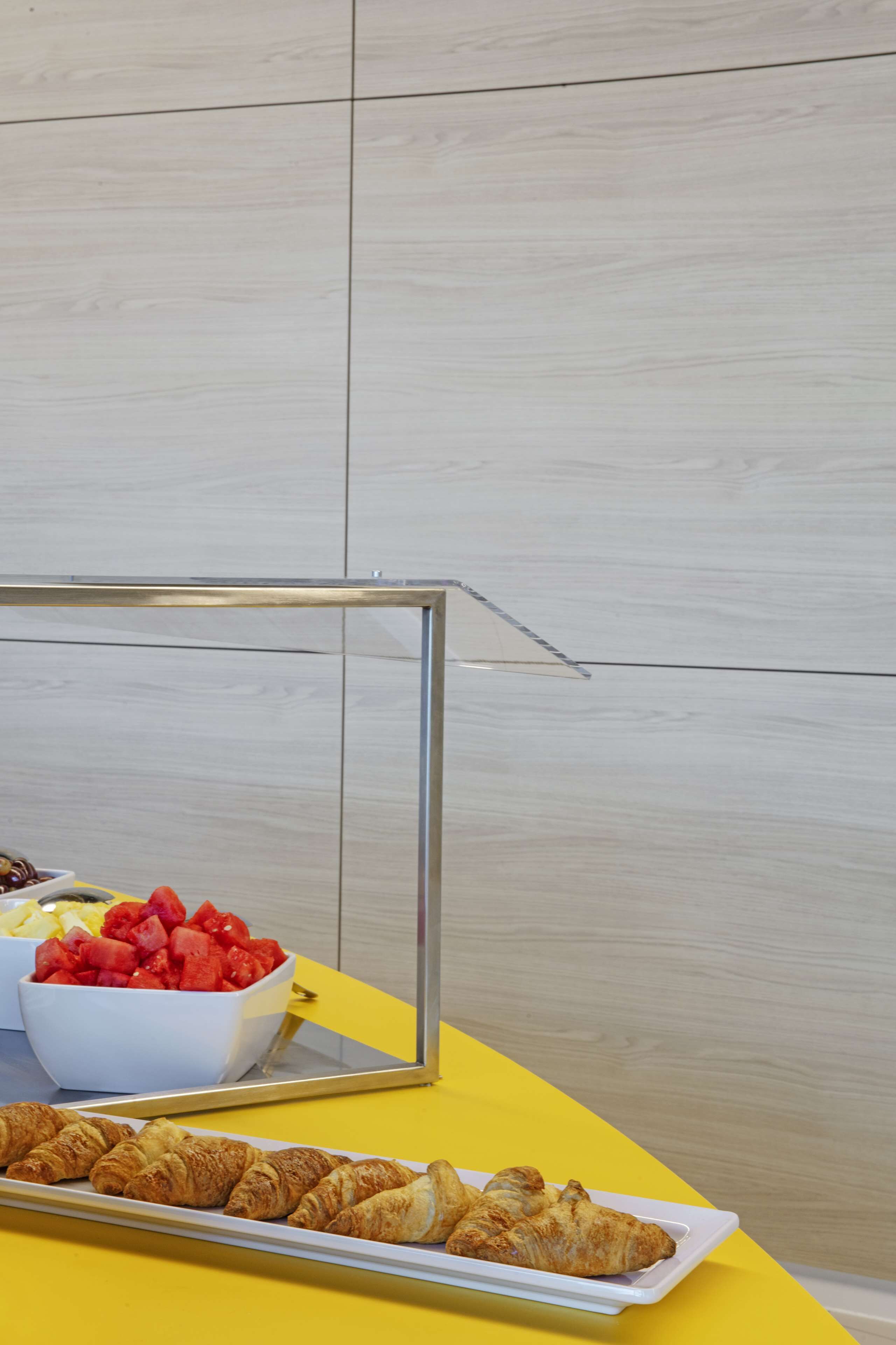 A yellow table with a tray of croissants and a bowl of fruit.
