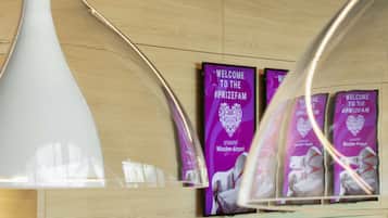 Ein Empfangsbereich mit modernem Design, mit einer großen weißen Vase und lila Willkommensschildern für die #PRIZEFAM Veranstaltung im Priezeotel München-Airport.