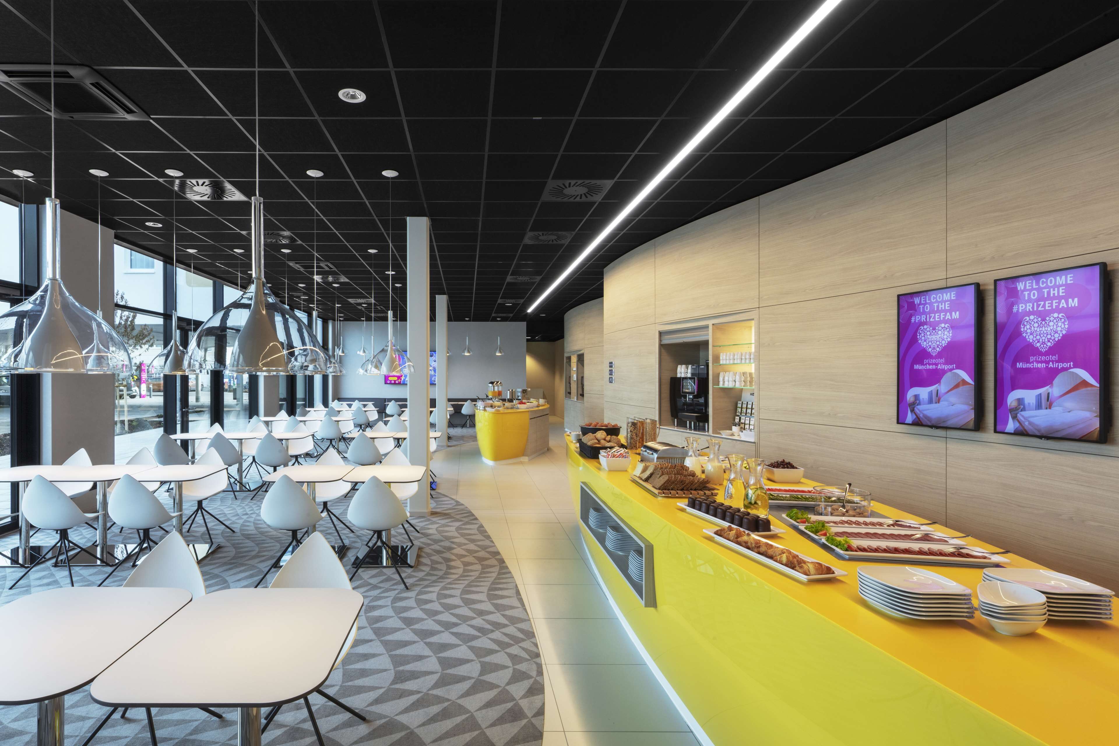 Una cafetería moderna con sillas blancas, un mostrador amarillo con comida y un ventanal grande.