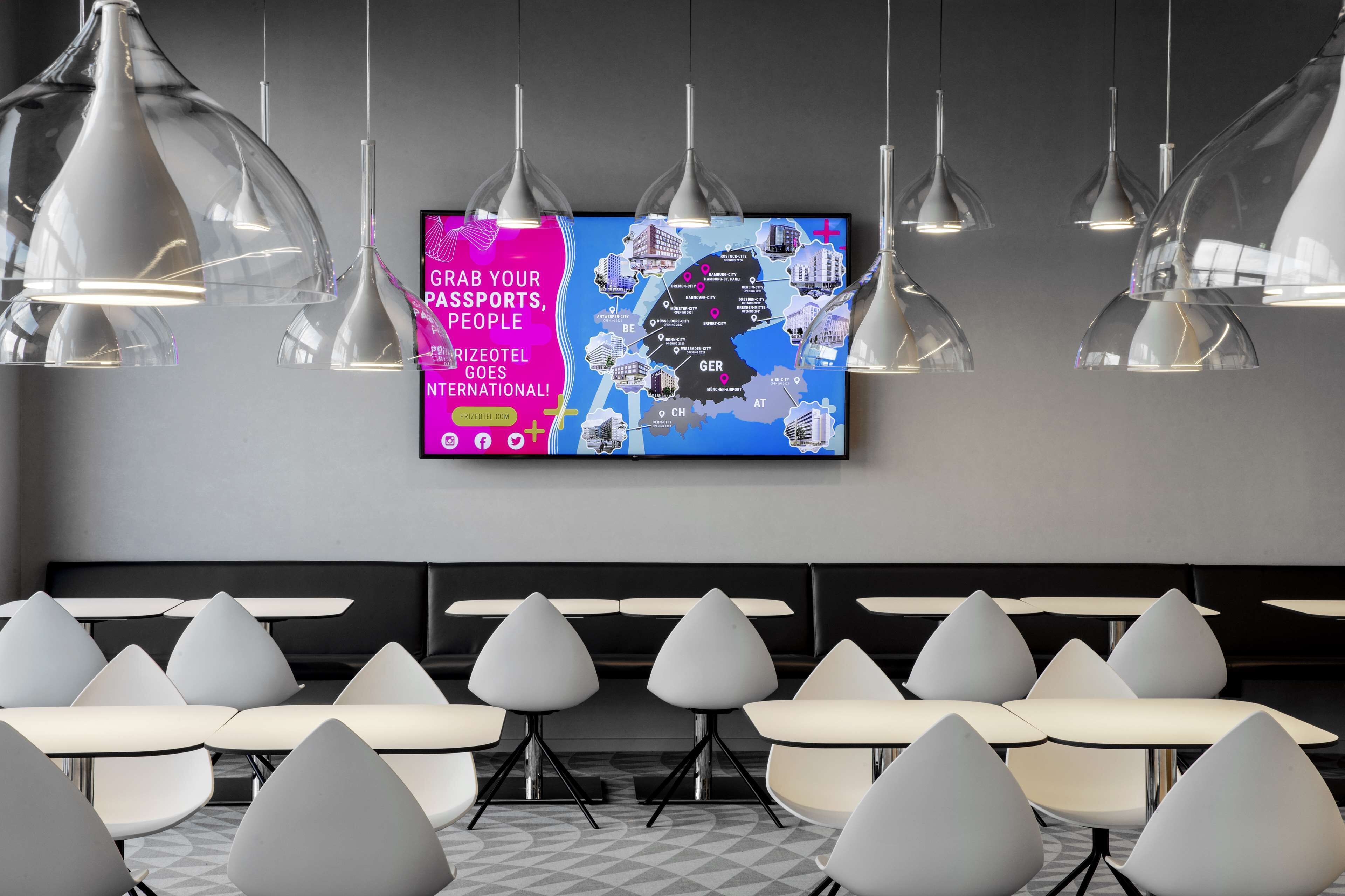 Un hall d’hôtel moderne doté d’un grand écran numérique affichant une carte, de plusieurs espaces de détente avec des fauteuils originaux et d’un éclairage suspendu.