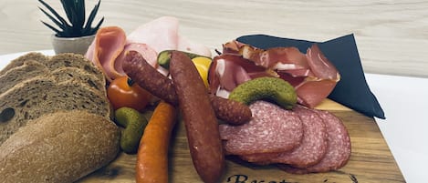 Una tabla de madera con diversos embutidos, quesos y encurtidos, con la etiqueta 'Brotzeit'.