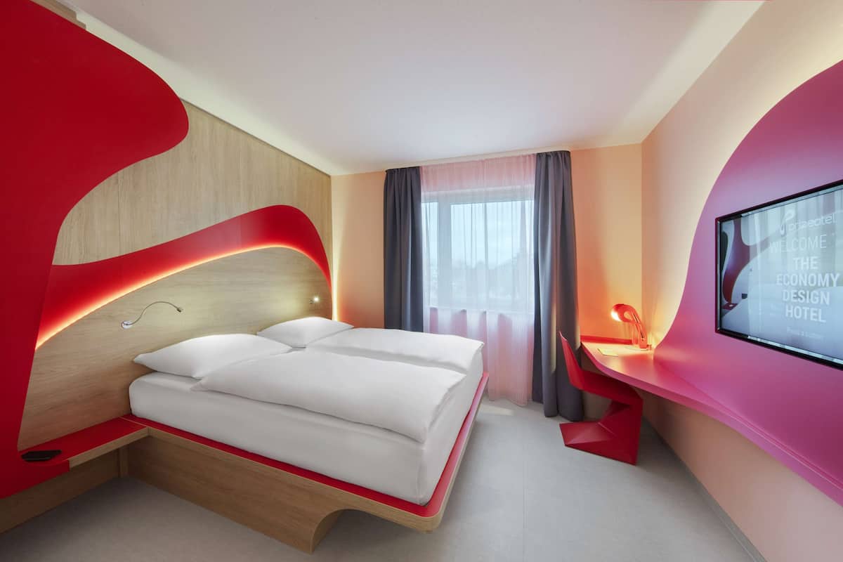 Una habitación de hotel moderna con una cama, un escritorio y un ventanal grande.