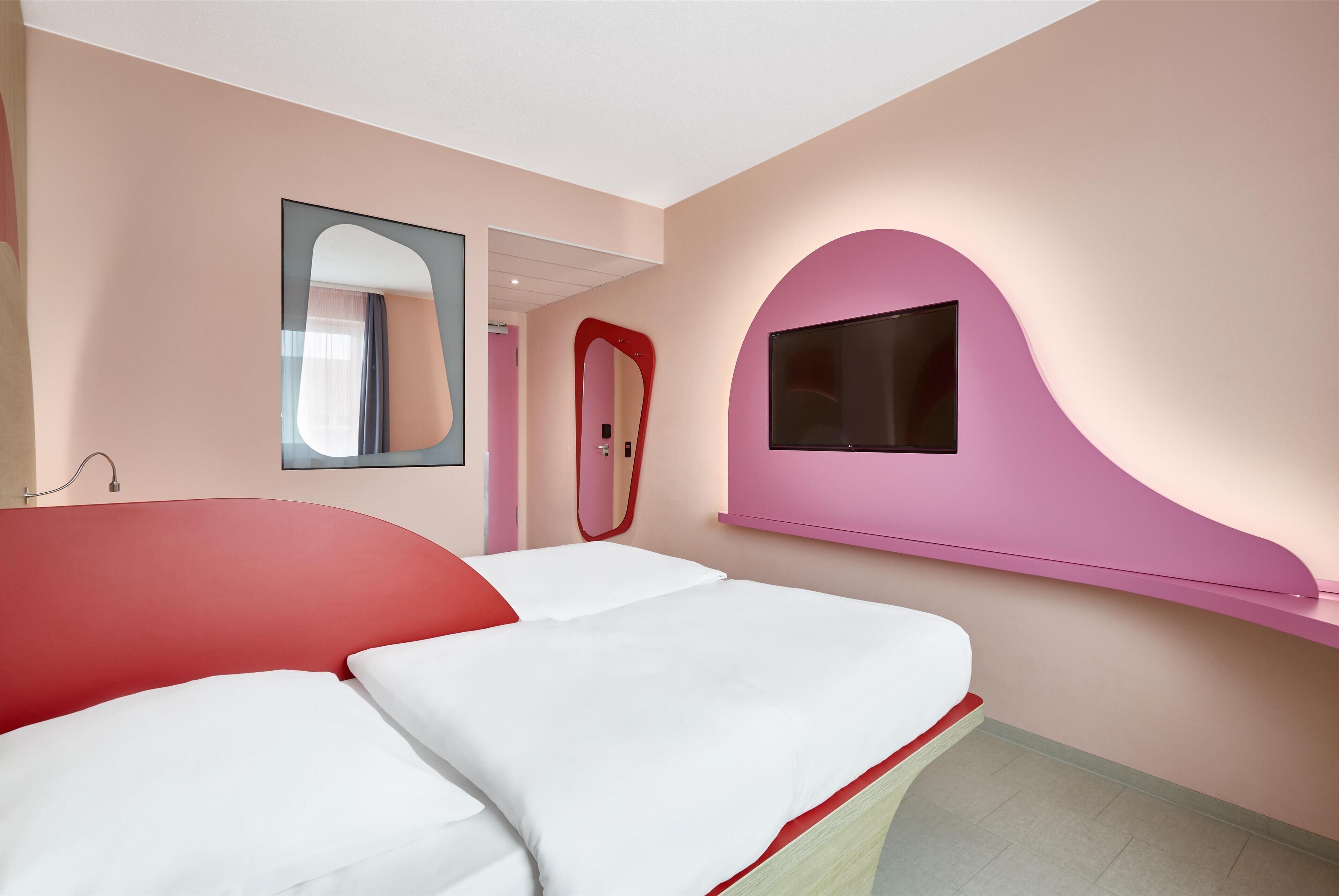 Una habitación de hotel moderna con una cama grande, un televisor montado en la pared y un espejo.
