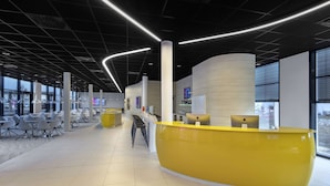 A modern reception area with a curved yellow desk, white chairs, and a clean, minimalist design. - Prize by Radisson, Munich Airport (Hallbergmoos)