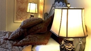 Una cama bien hecha con una colcha estampada, una lámpara decorativa sobre una mesita de noche y una obra de arte enmarcada en la pared.