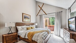 Ein Schlafzimmer mit einem hölzernen Bett, einem Nachttisch, einem Fernseher und Blick ins Freie.