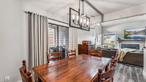 Ein Essbereich mit Holztisch und Stühlen, einer Chandelüster und Blick auf das Wohnzimmer.