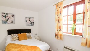 A neatly arranged bedroom with a bed, a nightstand, a radiator, and a window with curtains. - Brunston Castle (Girvan)