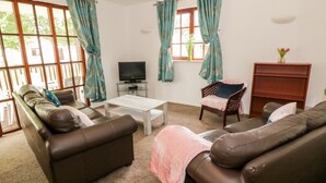 A living room with a brown leather sofa, a white coffee table, a television on a glass stand, and a window with teal curtains. - Brunston Castle (Girvan)
