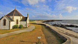 A coastal church with a gravel path leading to it, a signpost, and a rocky shoreline.