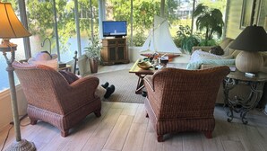 A cozy living room with wicker furniture, a television on a cabinet, and a view of a lake through large windows. - Come and enjoy NAPLES Florida a slice of paradise (Naples)