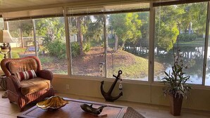 A room with a large window overlooking a garden and a body of water, a wicker chair, a decorative anchor, and a potted plant. - Come and enjoy NAPLES Florida a slice of paradise (Naples)