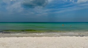 A beach with clear turquoise water, a sandy shore, and a partly cloudy sky.